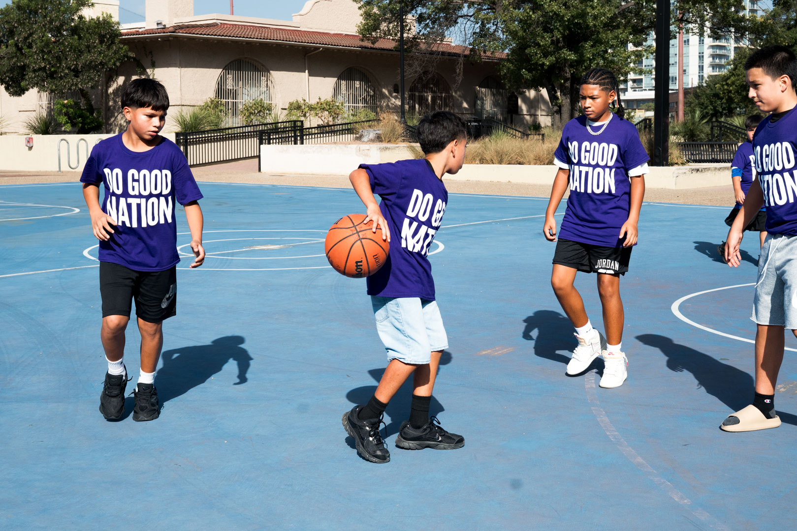 Kids in Do Good Nation shirts playing a pickup game on the outdoor court at the park
