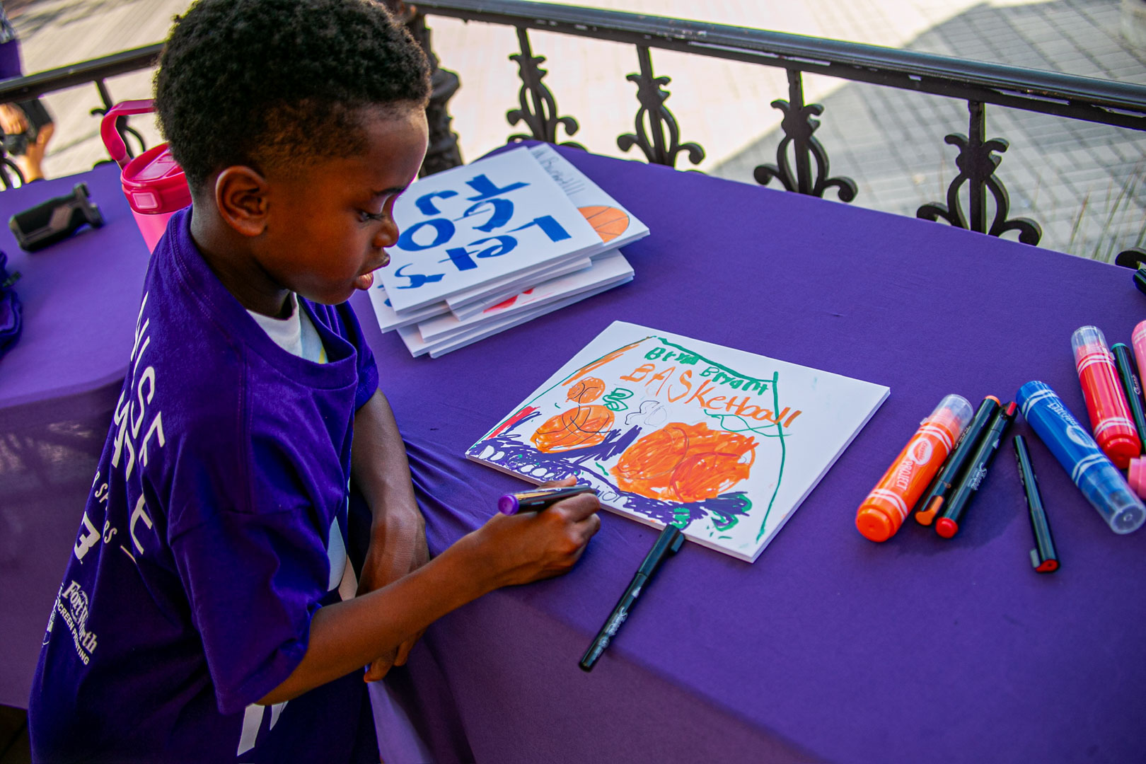 A boy drawing his own basketball sign in marker at the sign making table