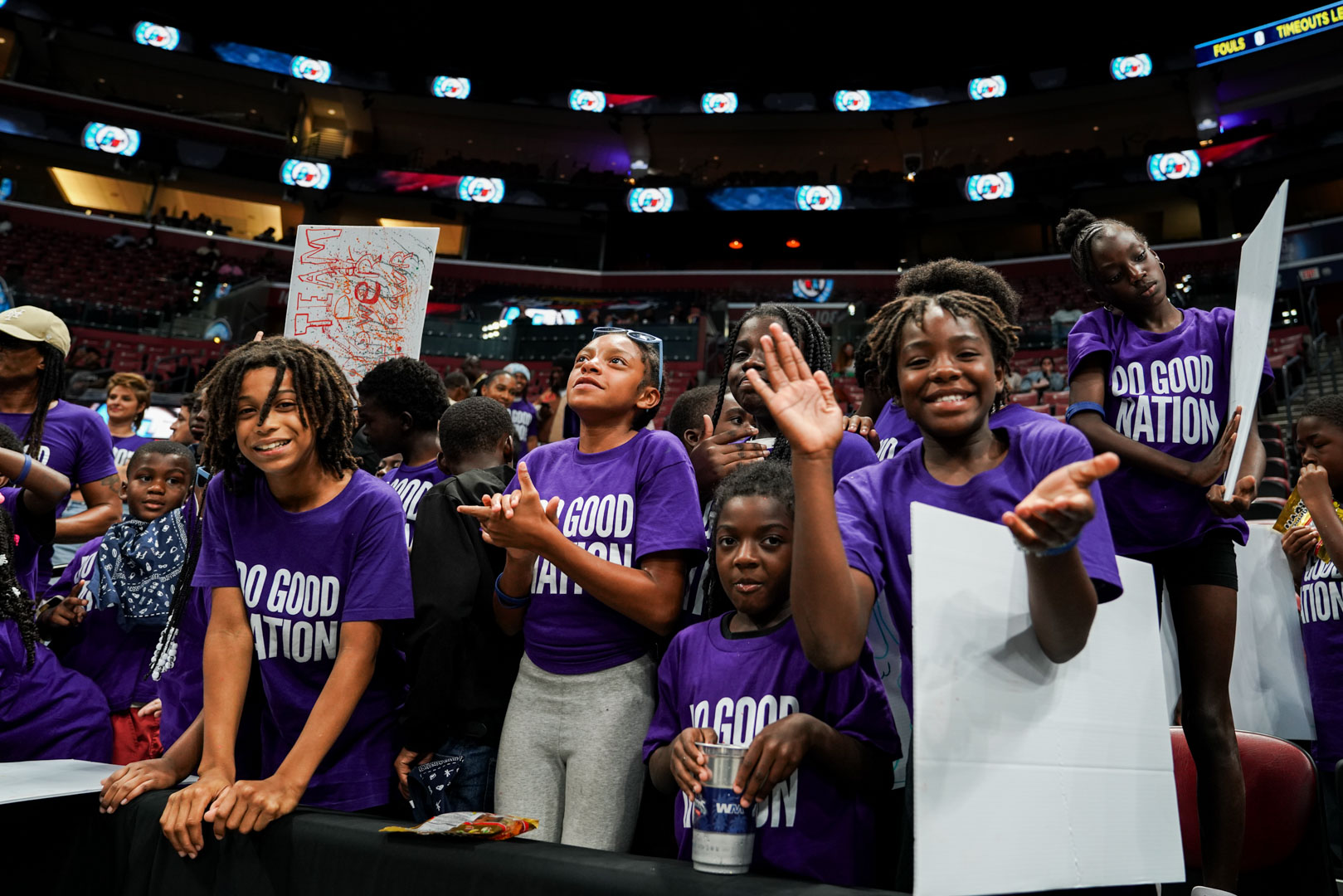 Youth in Do Good Nation shirts at the rail in The Impact Section, cheering and holding the signs they made